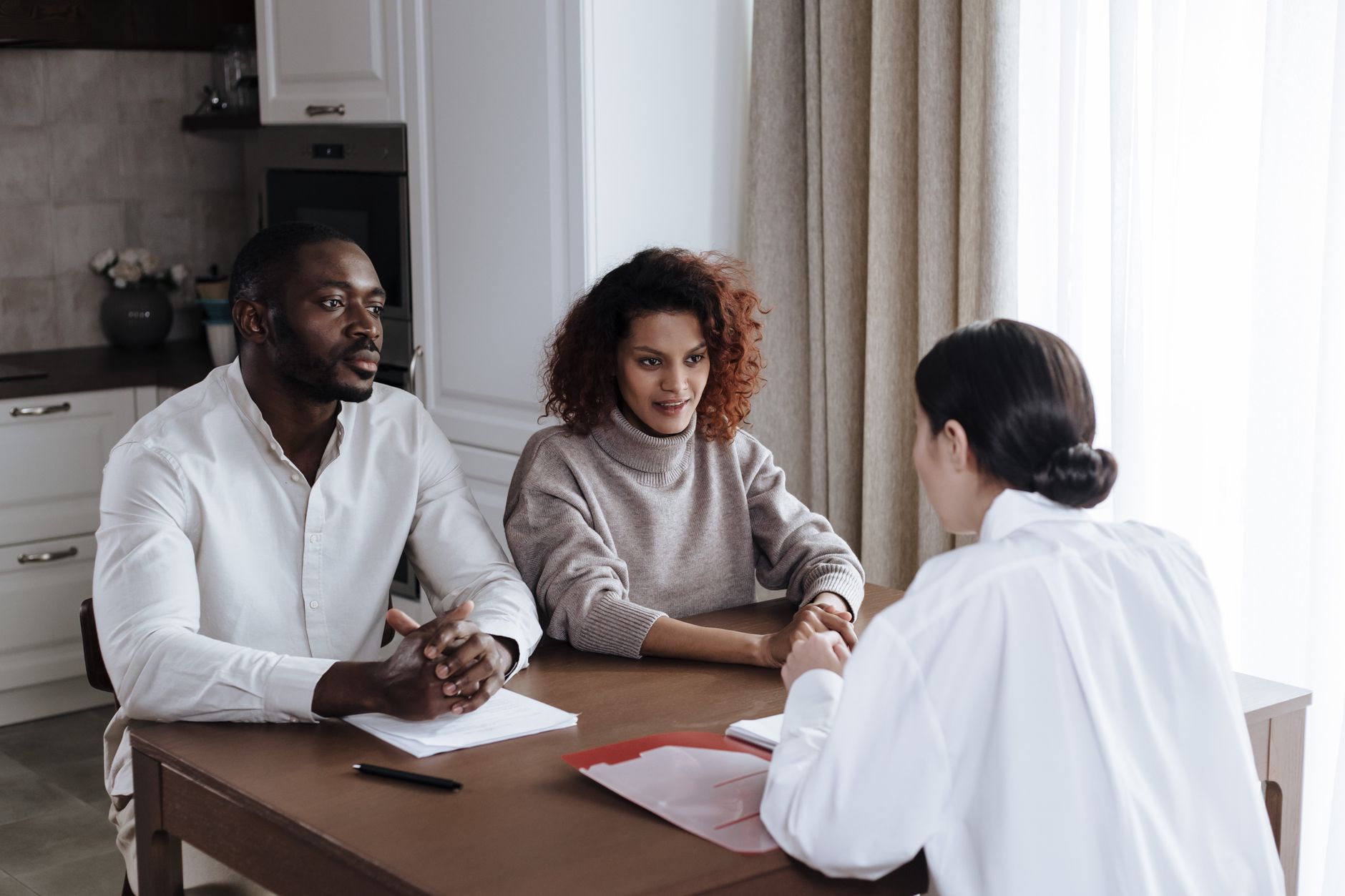 A social worker with a red folder meets a couple at their kitchen table to go over paperwork