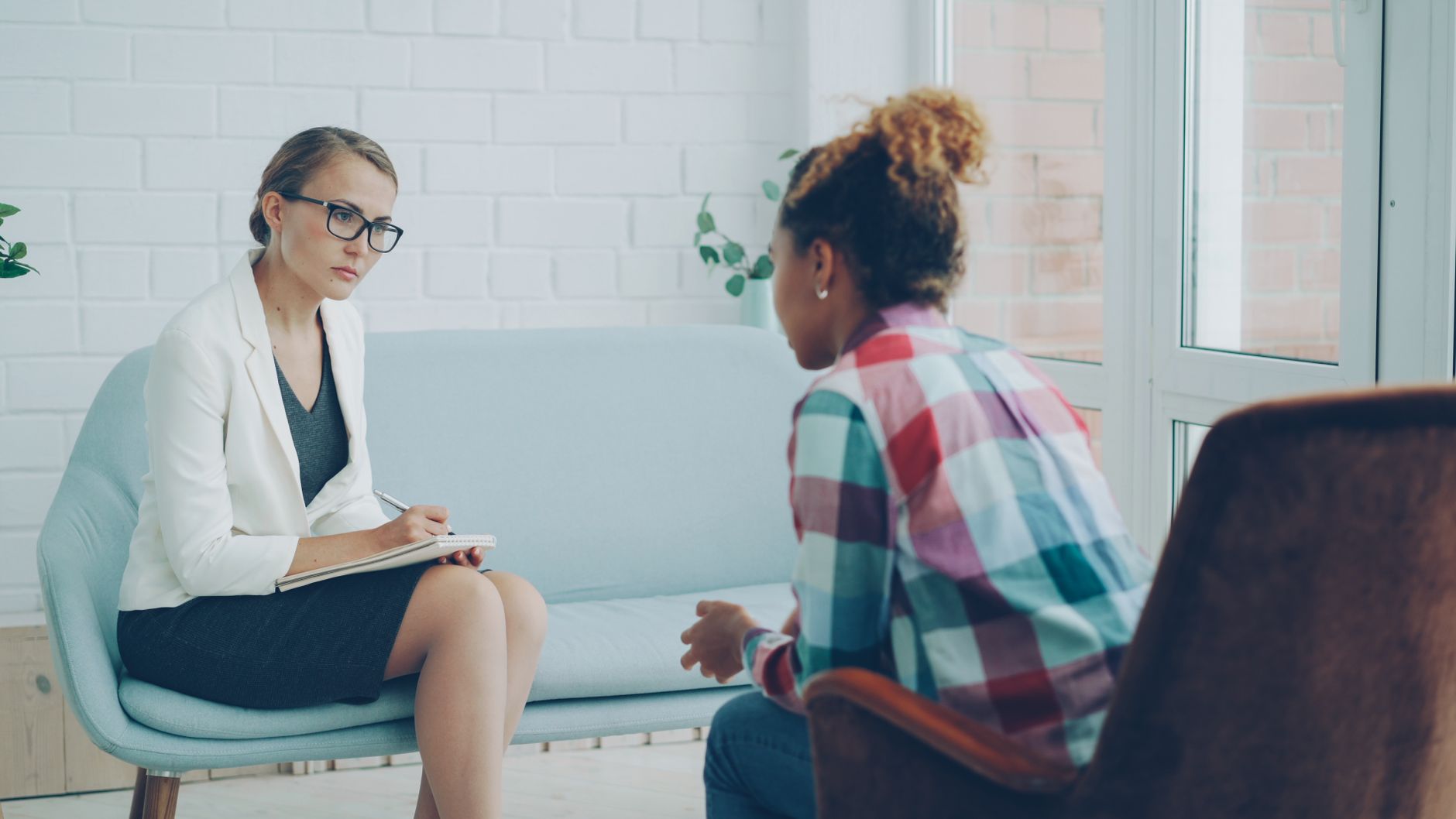 A clinician with a notebook listens to a client during a counseling session in a bright office