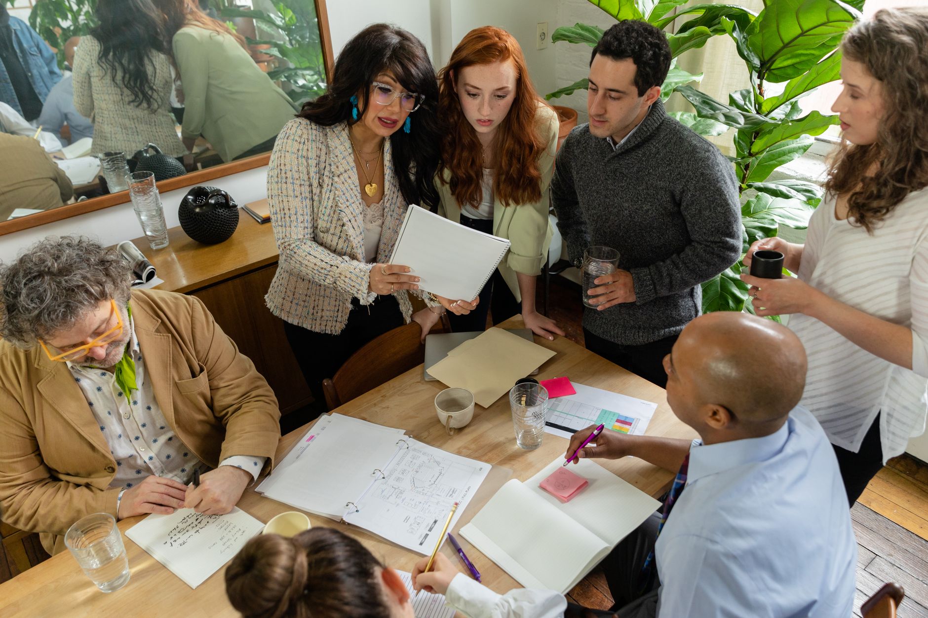 A group of colleagues gathers around a table covered with binders, notes and planning documents
