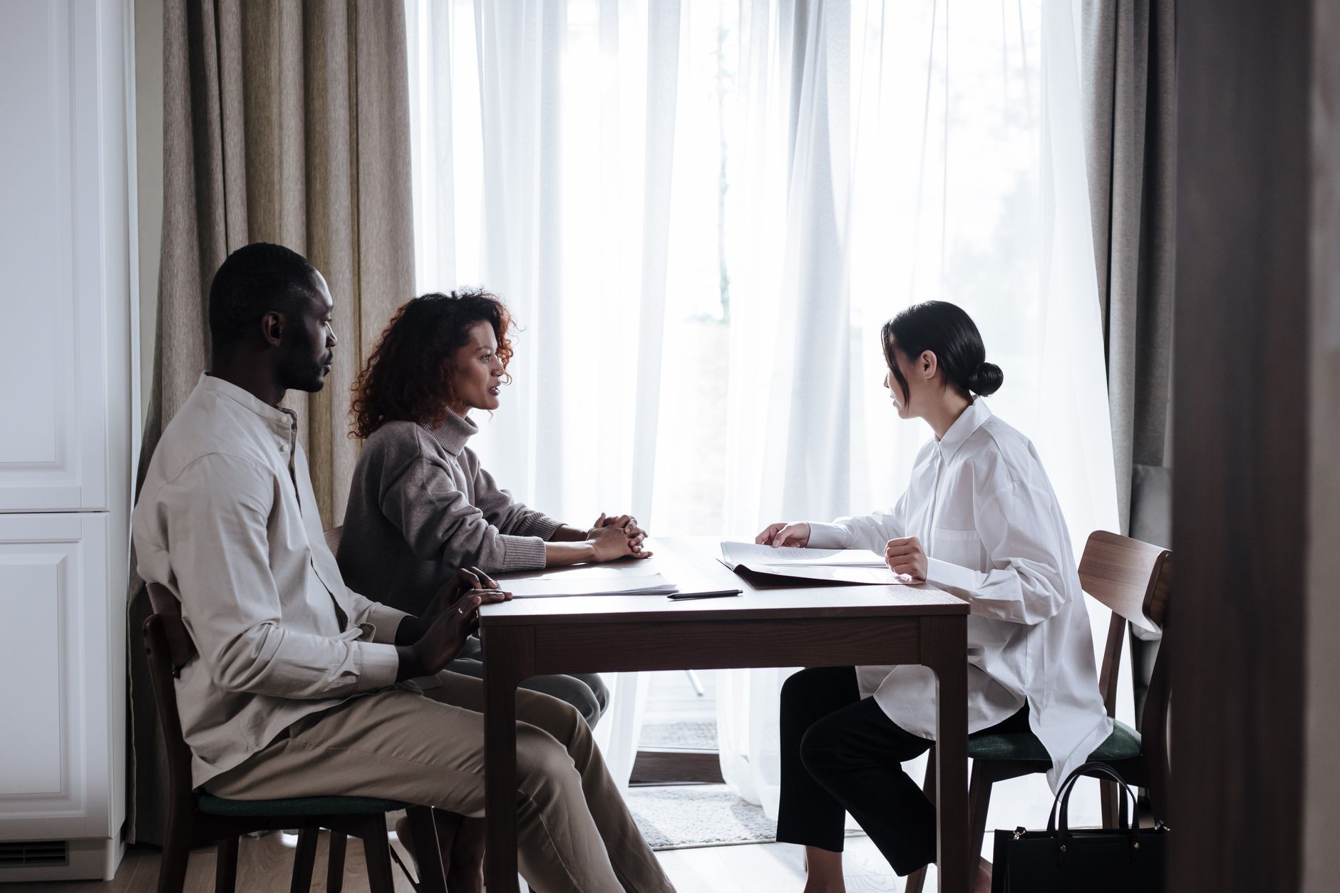 A social worker in a white shirt reviews papers at a table with a couple seated across from her